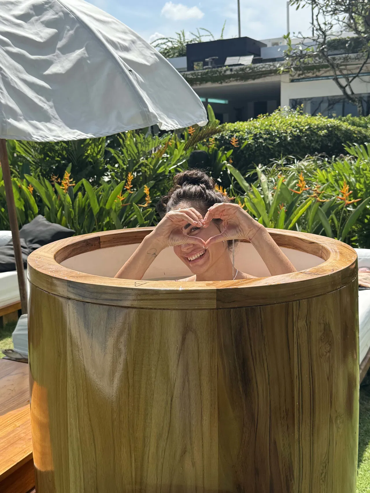 A joyful individual enjoying a handcrafted teak ice bath, embracing the benefits of cold therapy in a serene outdoor setting.