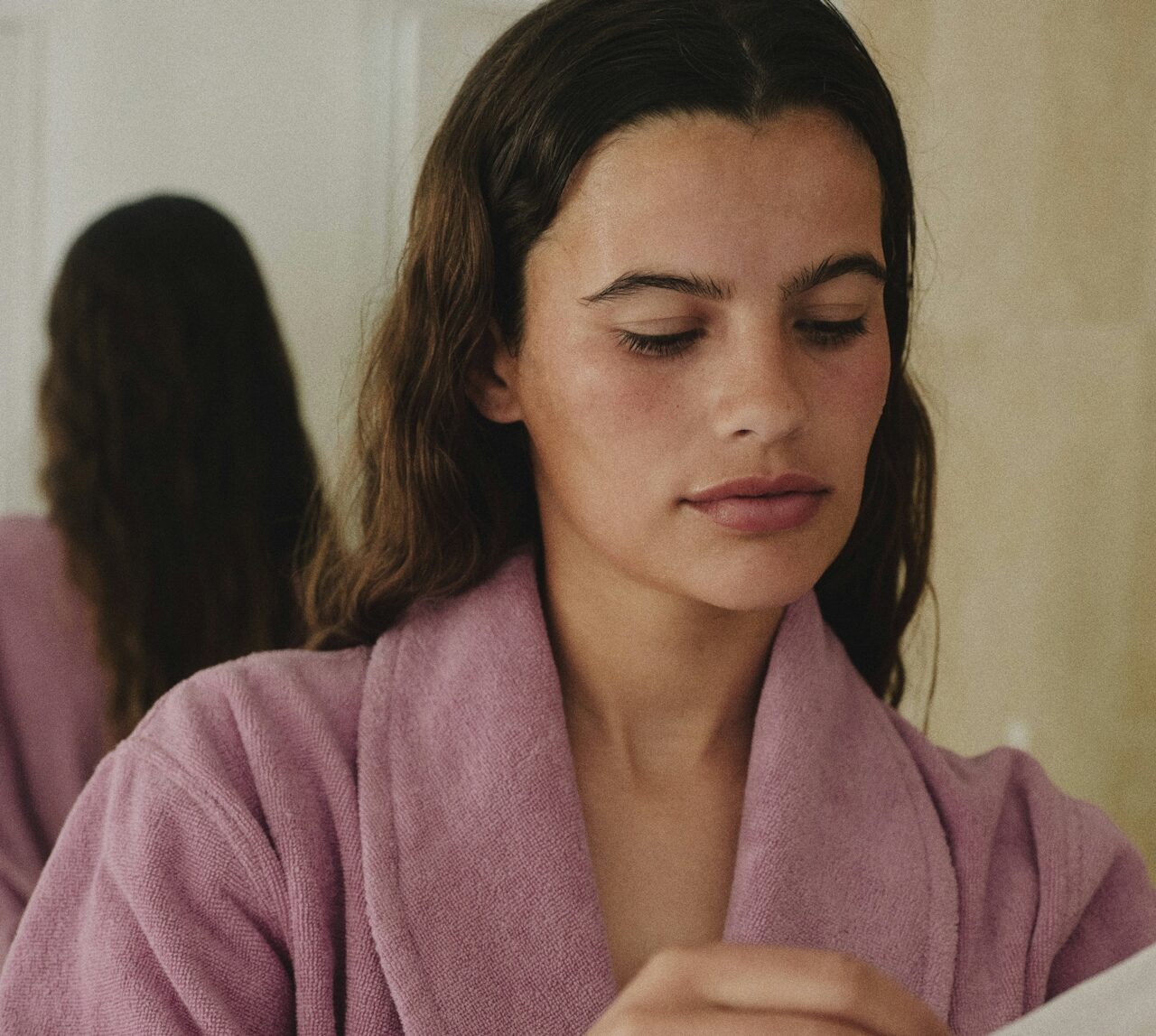 an attractive lady in a pink dressing gown prepearing to put a face mask on.