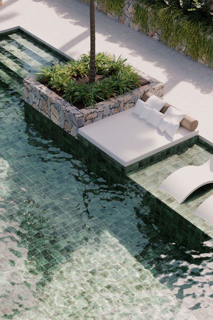 A pool with a double sunbed and green balinese stone tiles.