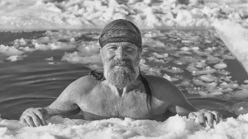 Black and White Photo of Wim Hoff coming out of a hole cut in a frozen lake.