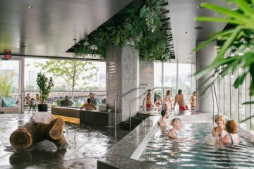 Spacious communal bathhouse interior with multiple thermal pools, steam, and warm ambient lighting, illustrating the social bathhouse business model.
