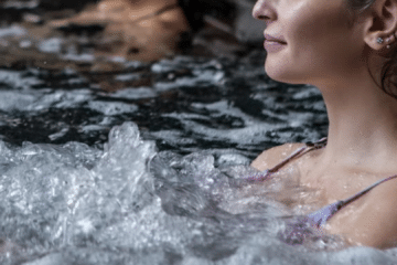 Close-up of a forearm resting on the edge of a cold plunge, water rippling in warm light