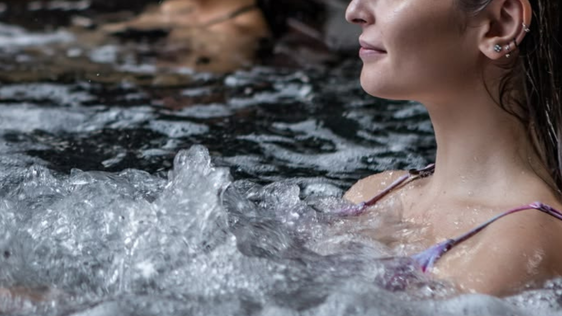 Close-up of a forearm resting on the edge of a cold plunge, water rippling in warm light