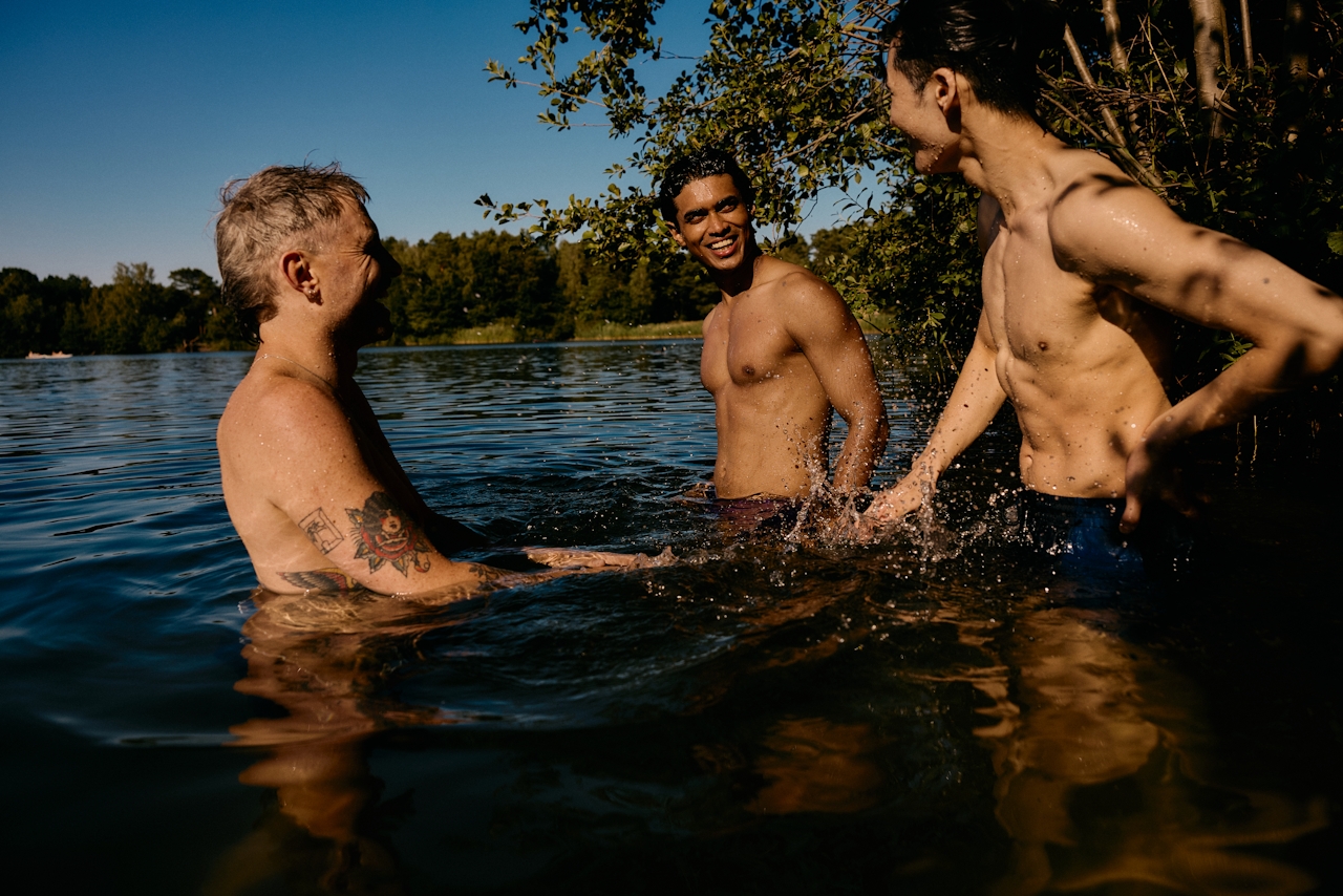 Three men laughing together in a lake at golden hour, water at chest level, the social side of cold water swimming