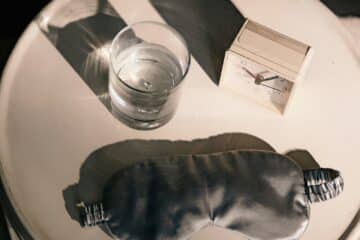 a bedside cabinet with a sleep mask, glass of water and alarm clock.