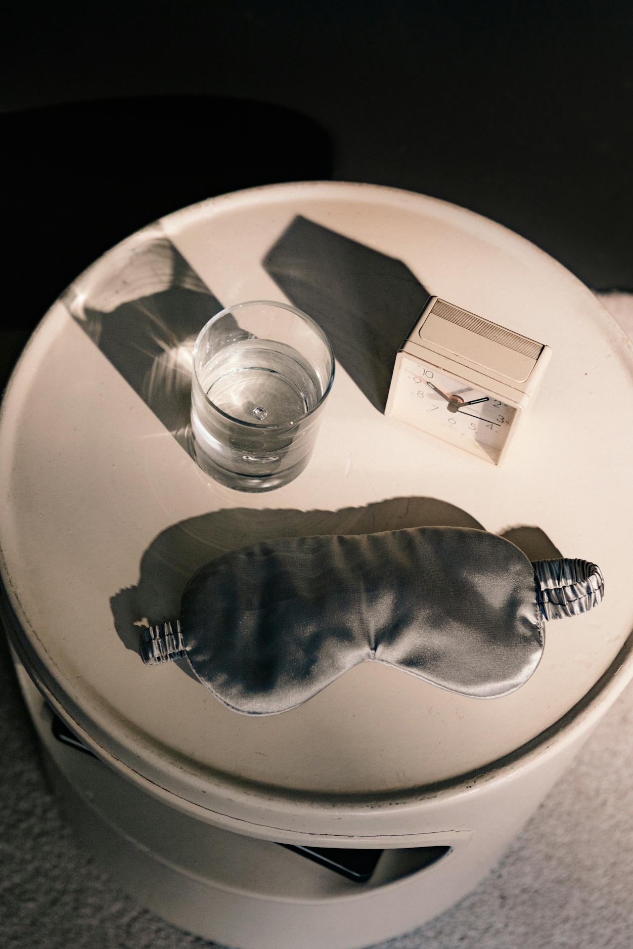 a bedside cabinet with a sleep mask, glass of water and alarm clock.