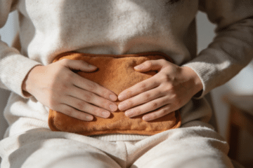 Close-up of hands resting over the lower abdomen with a warm compress, calm intimate image about women’s health and cold exposure.